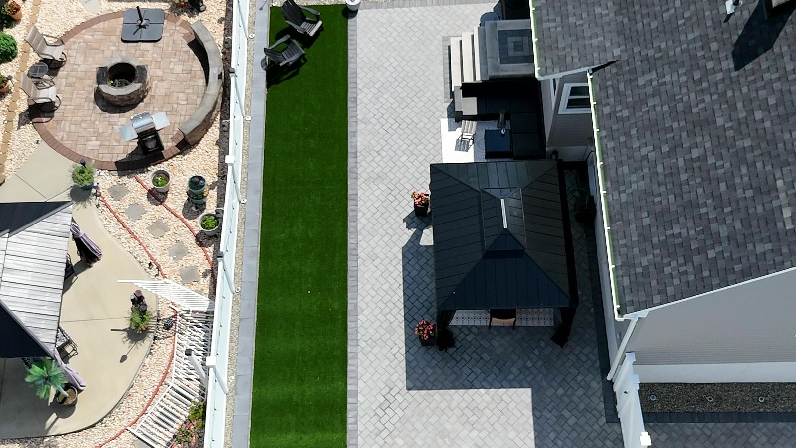 Aerial view of a finished backyard with a round paver patio, artificial turf and a retaining wall